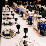 table set up with blue flowers and candles, black glasses