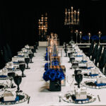 table set up with blue flowers and candles, black glasses and candles